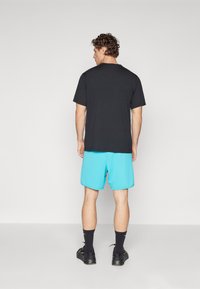 Camiseta de algodón negra, de manga corta, combinada con pantalones cortos azul claro. Calcetines negros hasta el tobillo y zapatillas negras visibles. Diseño sencillo, sin patrones.