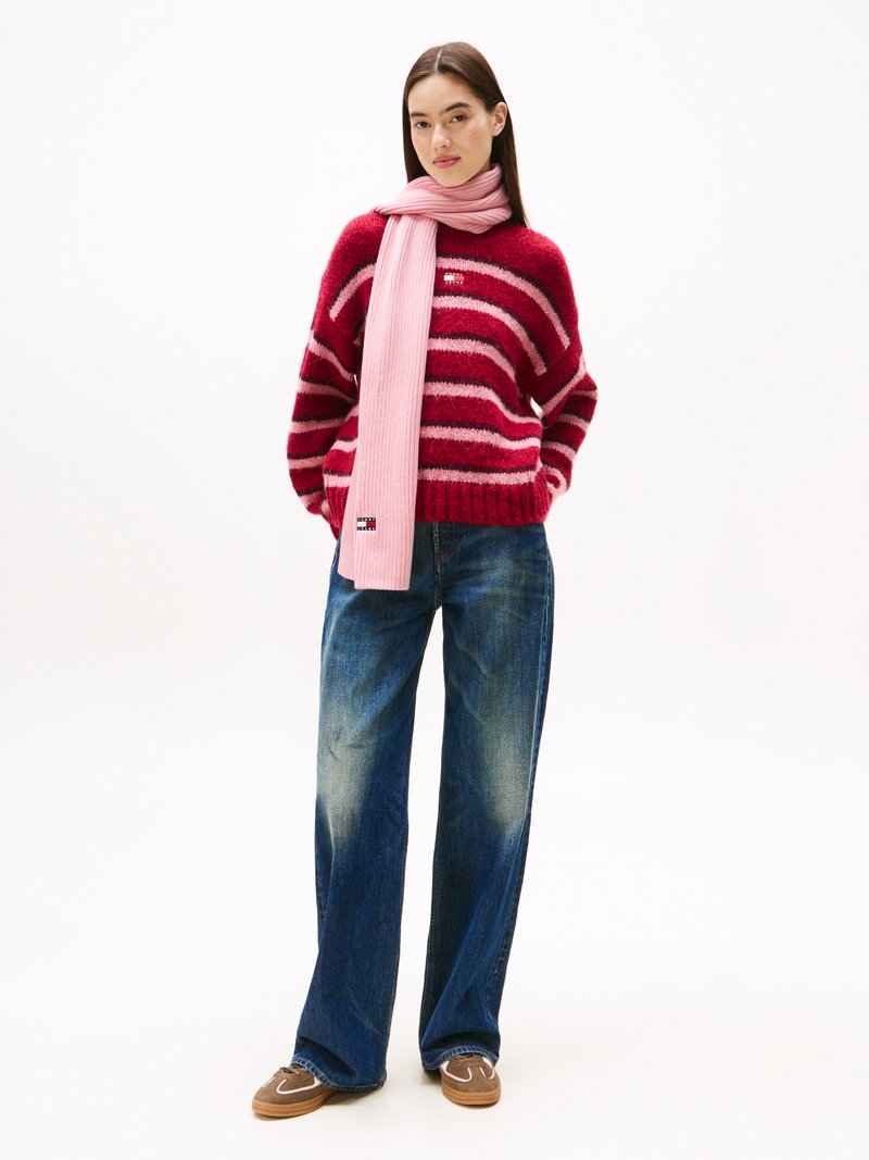 Maglione a righe rosse e rosa con scollo rotondo abbinato a jeans a gamba larga blu chiaro e una lunga sciarpa rosa chiaro. Scarpe marroni.
