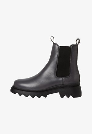 Black leather Chelsea boots with elastic side panels, chunky textured soles, and pull tabs for easy wear. Angular design with contrast accents.