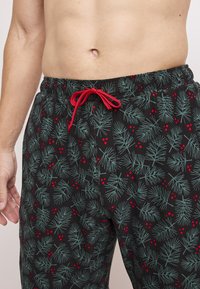 Svarta loungebyxor med ett mönster av tallblad och röda bär, elastisk midja med röd dragsko, bomullsmaterial, avslappnad passform.