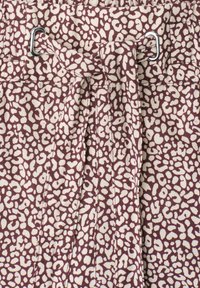 Gros plan d'une ceinture nouée à travers des boucles métalliques sur un tissu avec un motif tacheté irrégulier violet et beige.