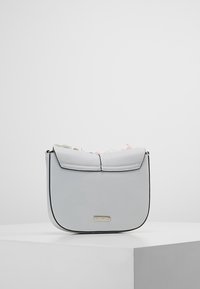 Šedá kabelka z umělé kůže s klopou, zaobleným tvarem, dekorativním prošíváním a jemným kovovým logem na přední straně.