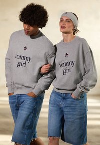 Felpe grigie con il testo "tommy girl" e un logo a stella; abbinate a pantaloni bermuda in denim. Tessuto morbido e vestibilità rilassata.