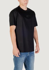 T-shirt nera a maniche corte con scollatura rotonda e una piccola etichetta sul petto, abbinata a jeans in denim azzurro chiaro.