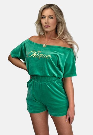 Grünes Samt-Oberteil mit schulterfreien Schnitt und goldfarbigem "Chique"-Schriftzug, kombiniert mit passenden Shorts mit elastischem Bund, glatte Textur, lockere Passform.