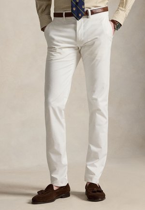 Homme portant un pantalon blanc slim, des mocassins à pampilles en daim marron, une ceinture marron, une chemise beige rayée, une cravate bleu marine à motifs et une montre-bracelet.