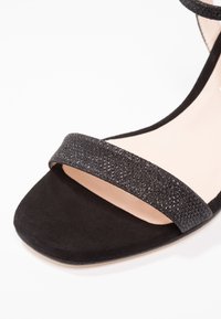 Sandale à talon haut en daim noir avec une large bride scintillante sur le dessus, dotée d'une semelle intérieure beige lisse et d'un bout carré.