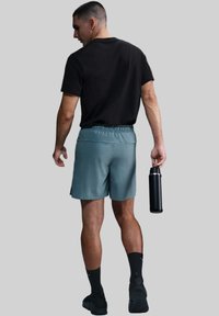 Sportsoutfit bestående af en sort t-shirt, lyseblå shorts med elastisk talje, sorte sokker og en sort vandflaske holdt i hånden.