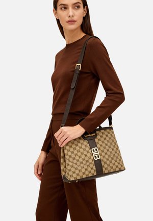 Borsa beige a motivo decorativo con tracolla in pelle marrone, dettagli dorati e un accento nero a contrasto con logo. Design morbido e strutturato.