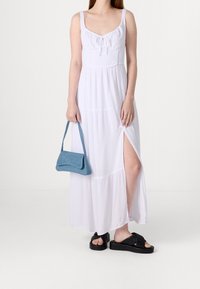 Vit maxiklänning med en figurnära överdel och spaghettistropper, med en sidoklaff. Kombinerad med en handväska i denim-stil i blått och svarta sandaler.