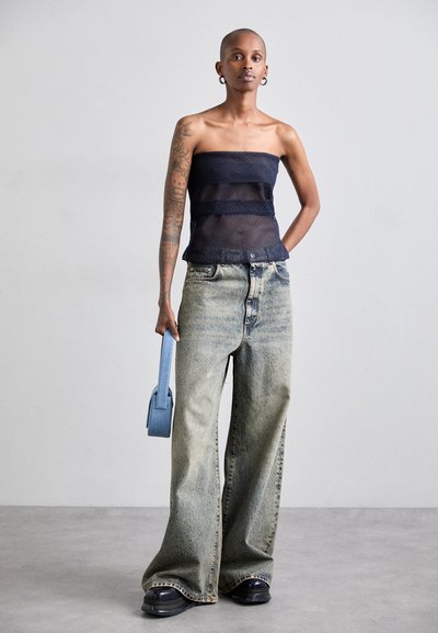 Top blu navy senza spalline con pannelli trasparenti, jeans a vita alta larghi e in denim chiaro, e una piccola borsa blu, abbinati a scarpe con piattaforma nere.