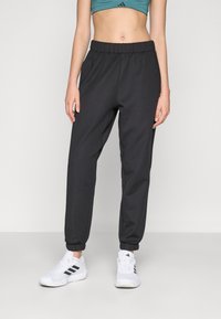 Mustad mustreeriga jogger-püksid, elastsest materjalist vöökoha ja sääreotsadega. Kombineeritud valgete spordijalatsitega, millel on mustad aktsendid.