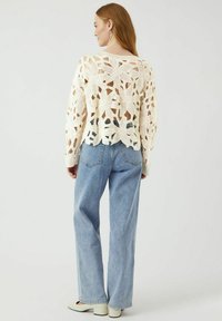 Virkat krämfärgat tröja med blommönster, lös passform. Kombinerat med ljusblå högmidjade jeans och krämfärgade klackskor.
