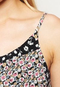Camiseta de tirantes con estampado floral que presenta un fondo negro con flores en tonos rosa, crema y marrón, tirantes finos y una textura suave.