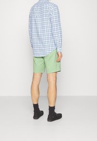 Ljusblå och vit rutig skjorta med lång ärm, gröna shorts, svarta skor och mörka strumpor. Fokusera på skjortans mönster och färgkontrast.