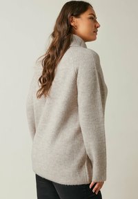 Maglione a coste grigio chiaro con collo alto, spalle calate e spacchi laterali, realizzato in un tessuto morbido e testurizzato.