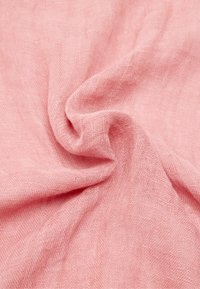 Miękki różowy materiał o luźnym splocie, delikatnie skręcony w centrum, tworzący miękkie fałdy i cienie.
