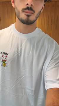 Bijela pamučna majica s kratkim rukavima, koja na lijevoj strani prsa ima šareni crtani grafički prikaz mačke s riječju "CHARM" iznad nje. Opusten kroj.