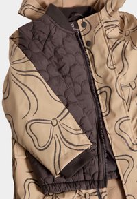 Polstret jakke med en blanding af beige og mørkebrune materialer, prydet med et blomster mønster, ribbede manchetter og en central lynlås.