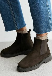 Bruine suède enkelboots met een zijrits, textuurstofpanelen en zwarte rubberen zolen. Gecombineerd met lichtblauwe cropped jeans.