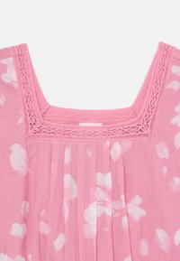 Blouse rose avec un décolleté carré agrémenté de dentelle, un motif floral et une texture plissée. Tissu léger et finition douce.
