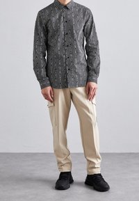 Maglietta a maniche lunghe a righe bianche e nere con colletto, abbinata a pantaloni cargo crema stretti sulle caviglie con tasche laterali e scarpe da ginnastica nere.