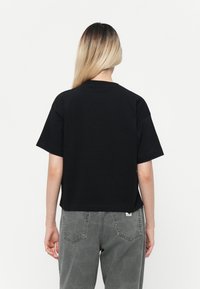 Black short-sleeve t-shirt with a loose, boxy fit. Soft cotton material, slightly cropped design, and a crew neckline. Gray pants visible.
