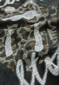 Close-up of wrinkled fabric with white distressed text and a brown and black leopard print pattern.