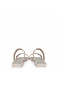 Sandalias planas con dos correas circulares, fabricadas con caucho beige suave. La suela es lisa y rectangular, con un diseño minimalista.