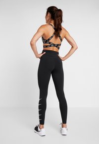 Leggings de sport noirs avec des détails en blanc, associés à un soutien-gorge de sport noir avec des bretelles croisées et le logo Nike.