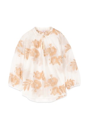 Blouse blanche transparente avec manches longues bouffantes, broderie florale beige, encolure ronde et fermeture à nouer avec pompon devant.