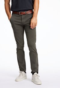 Olivgröna byxor i bomullsblandning, med en slim fit-design, framfickor och ett brunt läderbälte. Bärs med vita sneakers.