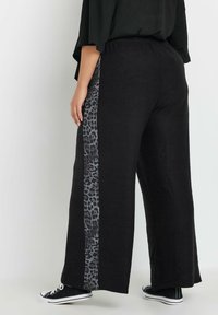 Czarne spodnie z szerokimi nogawkami z szaro-leopardowym paskiem po bokach; elastyczny pas i luźna faktura materiału; zestawione z czarnymi sneakersami.