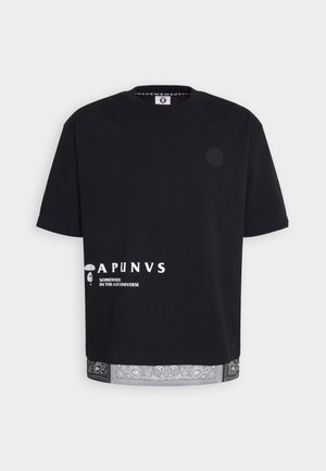 Czarna oversize'owa koszulka z białym napisem „APUNVS Somewhere in the Aape Universe” nadrukowanym u dołu oraz wykończeniem brzegu w wzór paisley.
