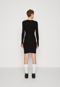 Robe en tricot côtelé noir à manches longues et design ajusté, arrivant au mi-cuisse. Portée avec des chaussettes blanches jusqu'aux genoux et des chaussures à plateforme noires.