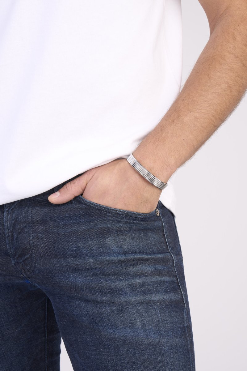 Silver mesh bracelet worn on the wrist, featuring distinct woven texture, set against a plain white t-shirt and blue denim jeans.