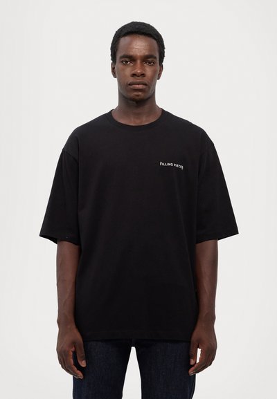 Svart bomull t-shirt med korta ärmar, med en liten vit "FILLING PIECES"-logotyp på vänster bröst. Klassisk rund krage.