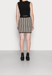 Schwarzes ärmelloses Oberteil und ein eng anliegender Minirock mit einem beigen und schwarzen geometrischen Muster, kombiniert mit schwarzen Stiefeletten.