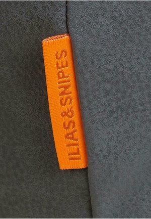 Grå stof med en struktureret overflade har et orange vævet mærkat med teksten "ILIAS & SNIPE." Mærket er placeret på sidekanten.