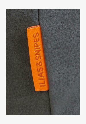 Grå stof med en struktureret overflade har et orange vævet mærkat med teksten "ILIAS & SNIPE." Mærket er placeret på sidekanten.