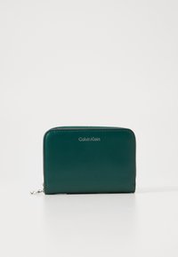 Green leather wallet with a zip closure, smooth texture, and silver "Calvin Klein" logo on the front, featuring a rectangular shape.