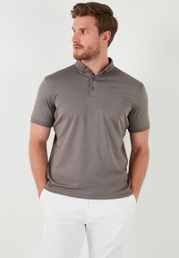 Šedé polo tričko s texturovaným povrchem, s třemi knoflíky a krátkými rukávy, doplněné o bílé kalhoty. Jednoduchý a moderní design.