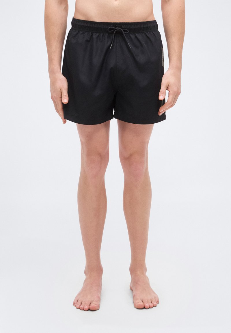 Μαύρα μαγιό βερμούδα με κορδόνι στη μέση, φτιαγμένα από ελαφρύ ύφασμα, με απλό σχέδιο και χωρίς ορατά μοτίβα ή διακοσμητικά στοιχεία.