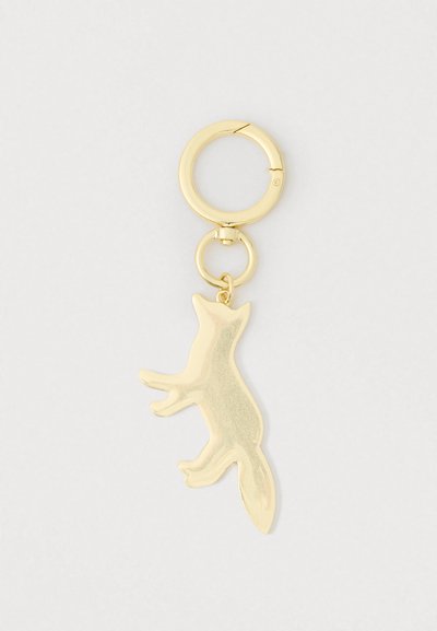 Χρυσό μπρελόκ με γυαλιστερό γοητευτικό φιόγκο σε σχήμα αλεπούς που κρέμεται από έναν κυκλικό κρίκο σε απλό ανοιχτό φόντο.