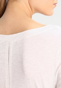 Valkoinen, kevyt t-paita, jossa on leveä pääntie ja näkyvä sauma selkäpuolella. Pehmeä kangas ja rento istuvuus.