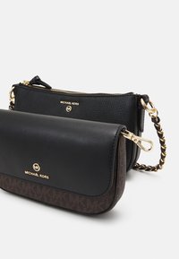 Deux sacs à main Michael Kors noirs, l'un avec une fermeture éclair et une chaîne dorée, l'autre avec un rabat et un logo sur une base marron à motifs.
