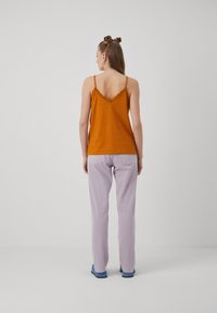 Oransje cami med blonder, parret med lyse lilla bukser, sett fra baksiden. Glatt stoff, spaghetti-stropper og avslappet passform.