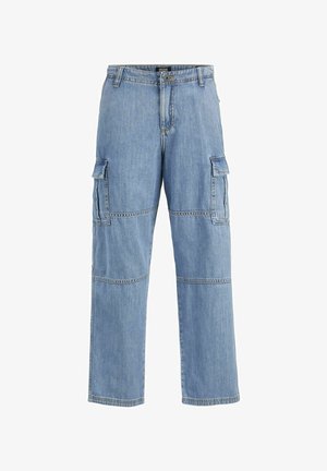 Jasnoszary oversize t-shirt z krótkim rękawem, w połączeniu z jasnoniebieskimi workowatymi dżinsami z kieszeniami cargo. Białe sneakersy z czarnymi akcentami.