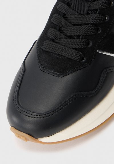 Tenis din piele neagră cu o secțiune din suede negru texturat, vârful rotund, șireți negri plat și o talpă contrastantă albă și de culoare gumă.