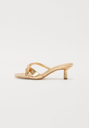 Gold metallic heeled sandals with a flat toe strap and a small, decorative floral accent. Slip-on design with a cushioned sole.
